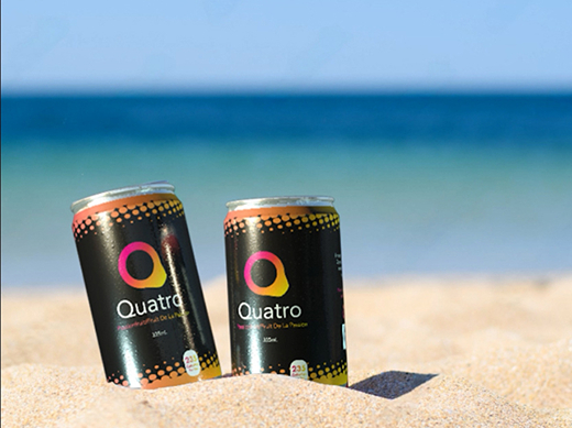 A picture of two cans of Quatro in the sand at the beach